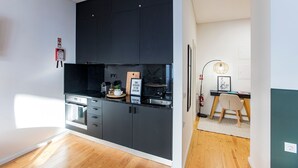 A modern kitchen with dark cabinets, a built-in oven, and a small dining area with a chair and table. - Mouzinho Studio w/ AC in City Center by LovelyStay (Porto)