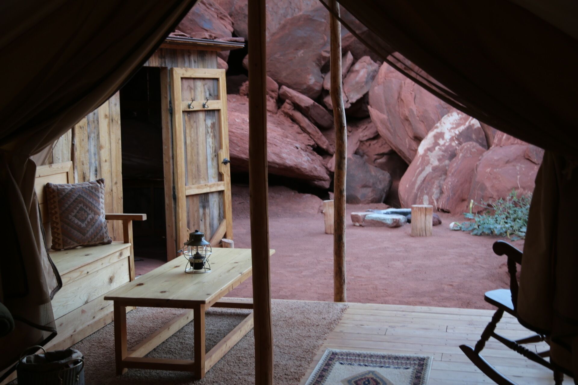 A rustic tent with a wooden table and a lantern, set against a backdrop of red rock formations.