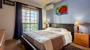 Un dormitorio con una cama, dos mesitas de noche con lámparas, una ventana con cortinas y un aire acondicionado de pared.