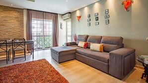 Una sala moderna con un sofá modular, una mesa de comedor con sillas y un amplio ventanal con cortinas translúcidas.