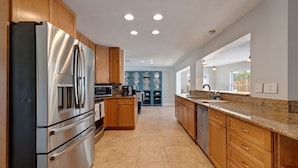 A modern kitchen with stainless steel appliances, wooden cabinets, and a granite countertop. - 511 Harbor Hideaway – Waterfront Retreat w/ Heated Pool, Dock, Golf Cart & Walk to Beach (Indian Rocks Beach)
