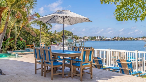 A patio with a table and chairs, a pool, and a view of the water. - 511 Harbor Hideaway – Waterfront Retreat w/ Heated Pool, Dock, Golf Cart & Walk to Beach (Indian Rocks Beach)