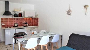A modern kitchen with white cabinets, a red-tiled backsplash, and a dining area with white chairs and a dark sofa.
