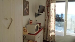 Une pièce avec un téléviseur fixé au mur, un four à micro-ondes posé sur un plan de travail, une décoration en forme de cœur et une fenêtre avec des rideaux.