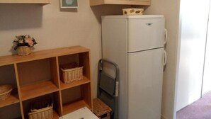 Une cuisine compacte avec un réfrigérateur blanc, des étagères en bois avec des paniers et une petite table.