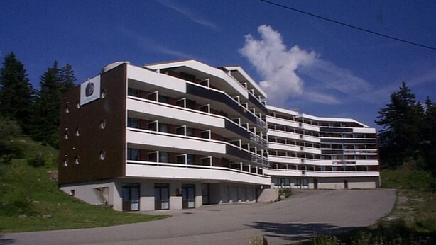 Un hôtel à plusieurs étages doté d’une architecture moderne, avec des balcons à chaque étage et une allée incurv ée menant à l’entrée.