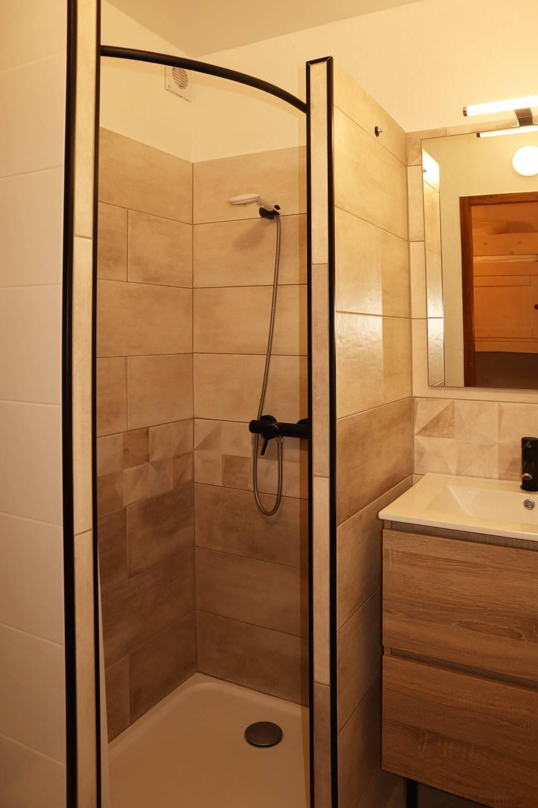 Una ducha con puerta de cristal, un lavabo blanco y un mueble de madera.