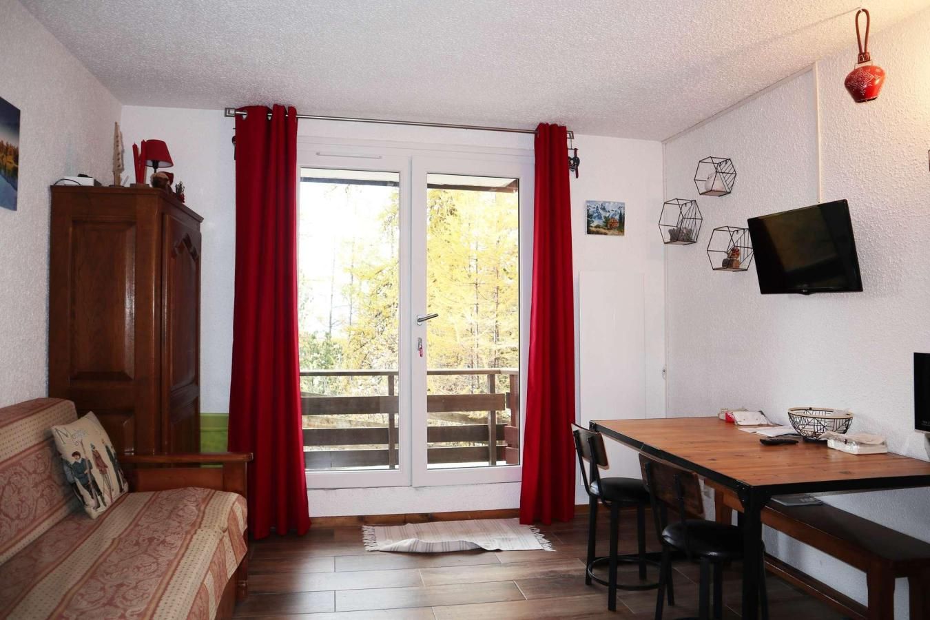 A room with a wooden dining table, chairs, a sofa, a wooden cabinet, and a TV on the wall.