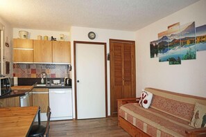 Ett kompakt bostadsutrymme med ett litet kök, en matplats och en soffa med en dekorativ prydnadskudde.