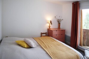 A bedroom with a bed, a bedside table with a lamp, a window with curtains, and a view of greenery outside. - 20m from ski slopes, 3rd floor, balcony, tv, 40m², Les Orres (Les Orres)