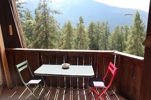 A balcony with a table and two chairs, overlooking a forested mountain area.