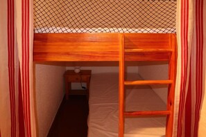 A bunk bed with a ladder, a nightstand with a lamp, and a striped curtain.