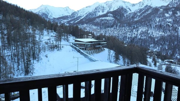 Et sneklædt bjerglandskab med en bygning, en skilift og en træterrasse i forgrunden.