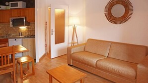En kompakt opholdsstue med et tekøkken, en sofa, et træbord og en lampe.
