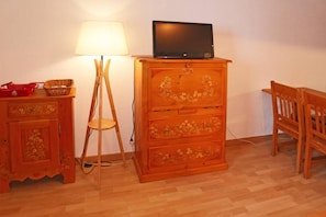 A room with a wooden cabinet, a lamp, a television on top, and a chair.