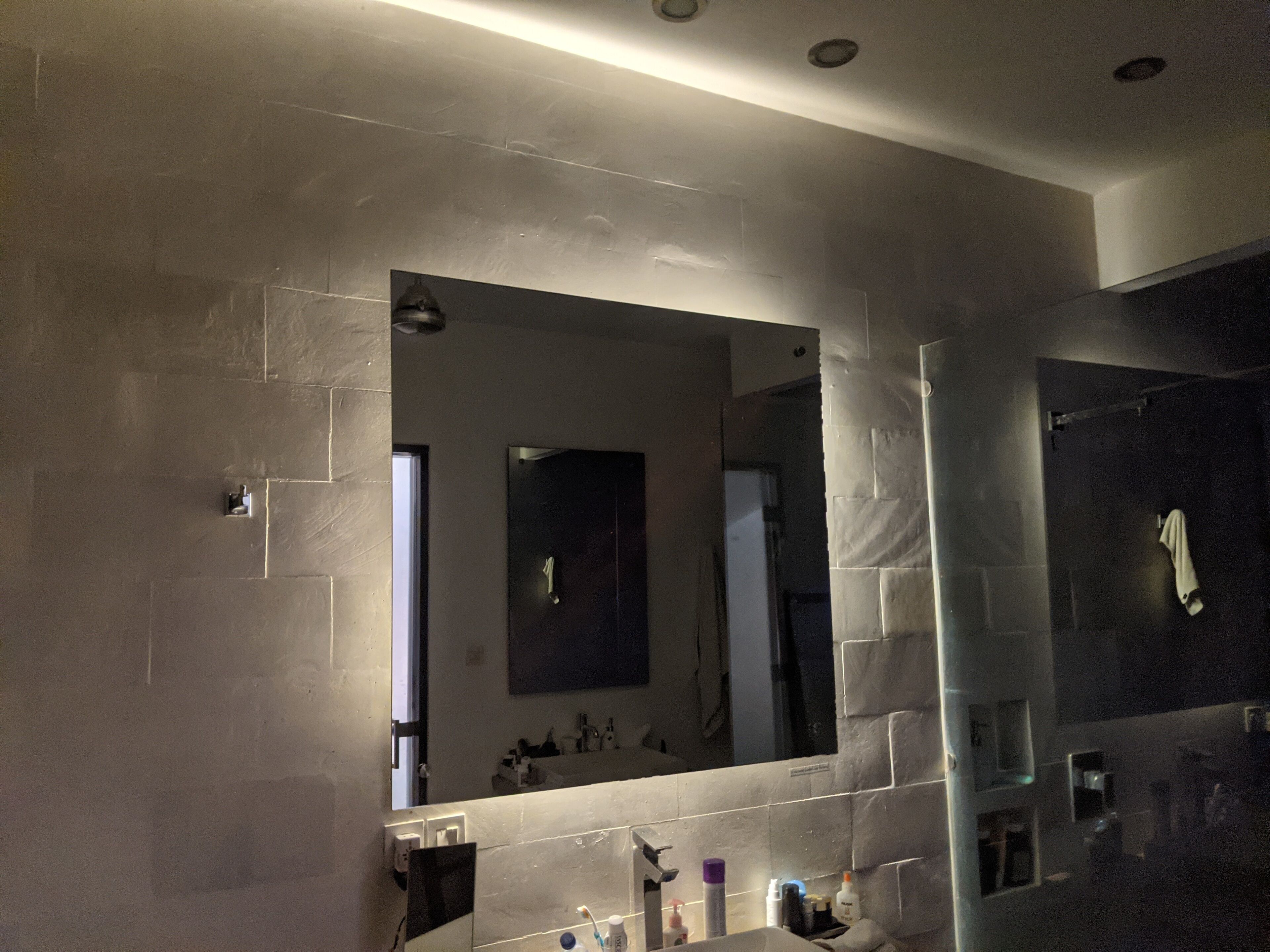 A bathroom with a large mirror, a sink, and toiletries.