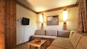 A cozy living room with a wooden floor, a beige sofa, a wooden coffee table, and a flat-screen TV mounted on the wall. - 150m from ski slopes, Ground floor, view valley, terrace, tv, ski locker, 24m², Montchavin La Plagne (La Plagne-Tarentaise)