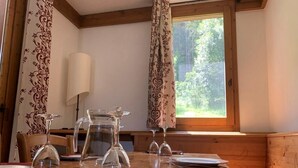 A dining table set with plates, cutlery, and a pitcher, with patterned curtains and a window with a view of greenery. - 150m from ski slopes, Ground floor, view valley, terrace, tv, ski locker, 24m², Montchavin La Plagne (La Plagne-Tarentaise)