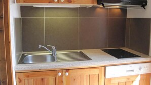 A compact kitchen with wooden cabinets, a stainless steel sink, a black induction cooktop, and a dishwasher. - 150m from ski slopes, Ground floor, view valley, terrace, tv, ski locker, 24m², Montchavin La Plagne (La Plagne-Tarentaise)