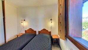 A room with two beds, wooden headboards, bedside tables, and a window with a view of a landscape. - 100m from ski slopes, 5th floor, view mountain, swimming pool, balcony, tv, ski locker, 31m² (Le Corbier)