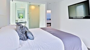 Ein Schlafzimmer mit einem Bett, einem an der Wand montierten Fernseher und Meerblick durch eine geöffnete Tür.