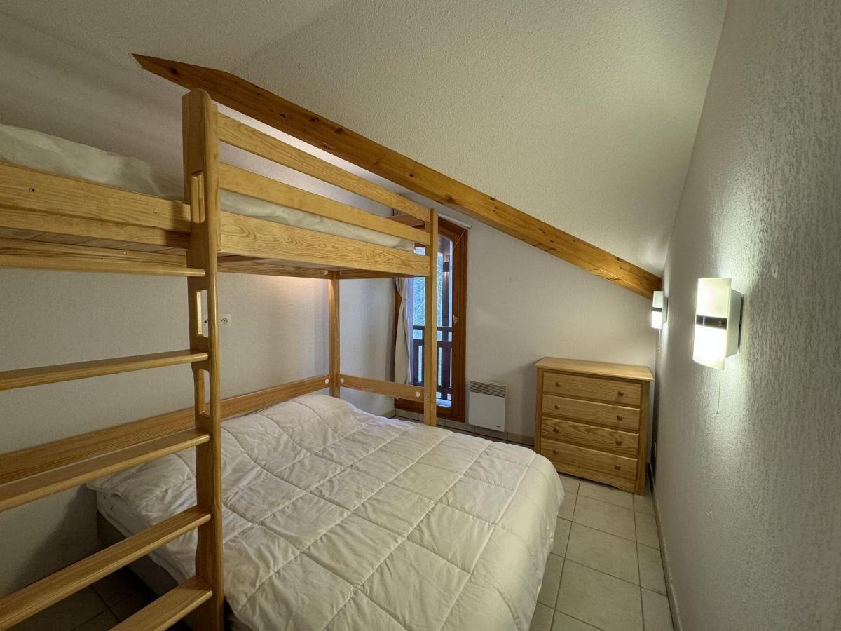Un dormitorio con una litera, un aparador de madera y una ventana con cortinas.
