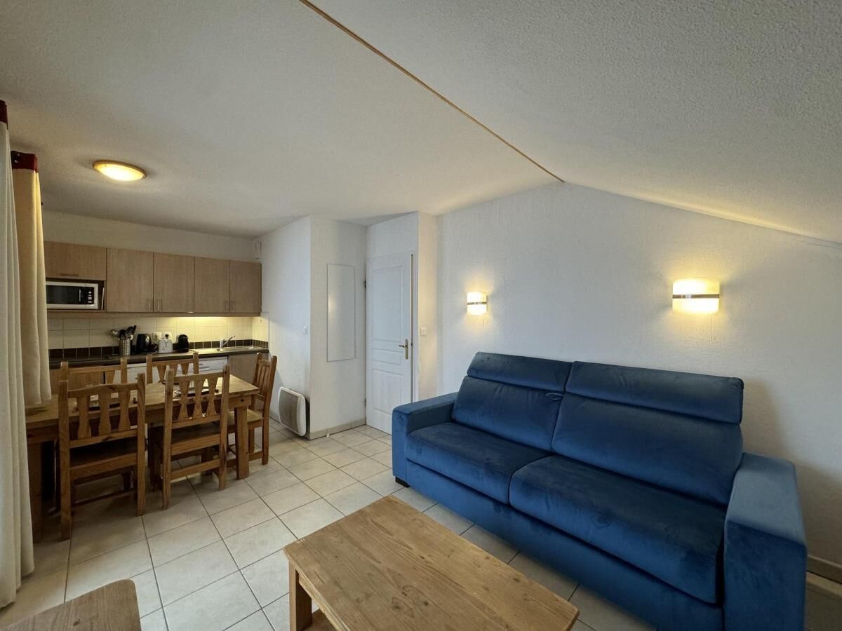 A compact living space with a kitchenette, a blue sofa, a wooden dining table, and a small coffee table.