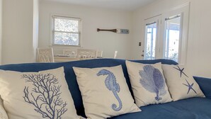 Un canapé bleu agrémenté de quatre coussins décoratifs aux motifs d’hippocampes et d’étoiles de mer.
