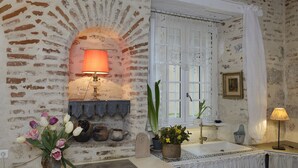Een rustieke badkamer met een bakstenen muur, een raam met kantgordijnen, een wastafel en een bloemenvaas.