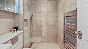 A modern bathroom with a shower, vanity, and a mirror with lights. - Cleveland Street by Aeria Apartments (London)