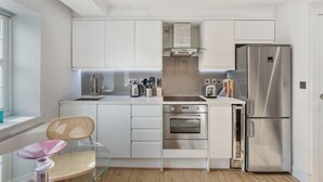 A modern kitchen with white cabinets, stainless steel appliances, and a glass dining table. - Cleveland Street by Aeria Apartments (London)