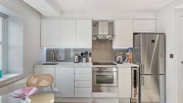 A modern kitchen with white cabinets, stainless steel appliances, and a glass dining table.