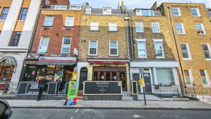 A row of multi-story buildings with various businesses on the ground floor, including a wine bar and a restaurant. - Cleveland Street by Aeria Apartments (London)