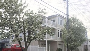 Una casa de dos pisos con un balcón, una camioneta roja estacionada adelante y una cerca blanca de piquetes.