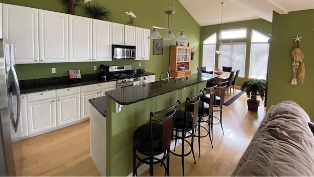 Una cocina con armarios blancos, encimera negra y una isla central con taburetes de bar.
