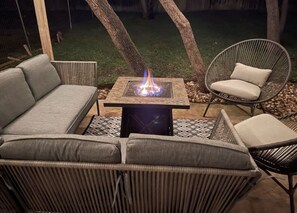 Un espacio de patio con una chimenea, una mesa y dos sofás de mimbre, además de una silla de mimbre.