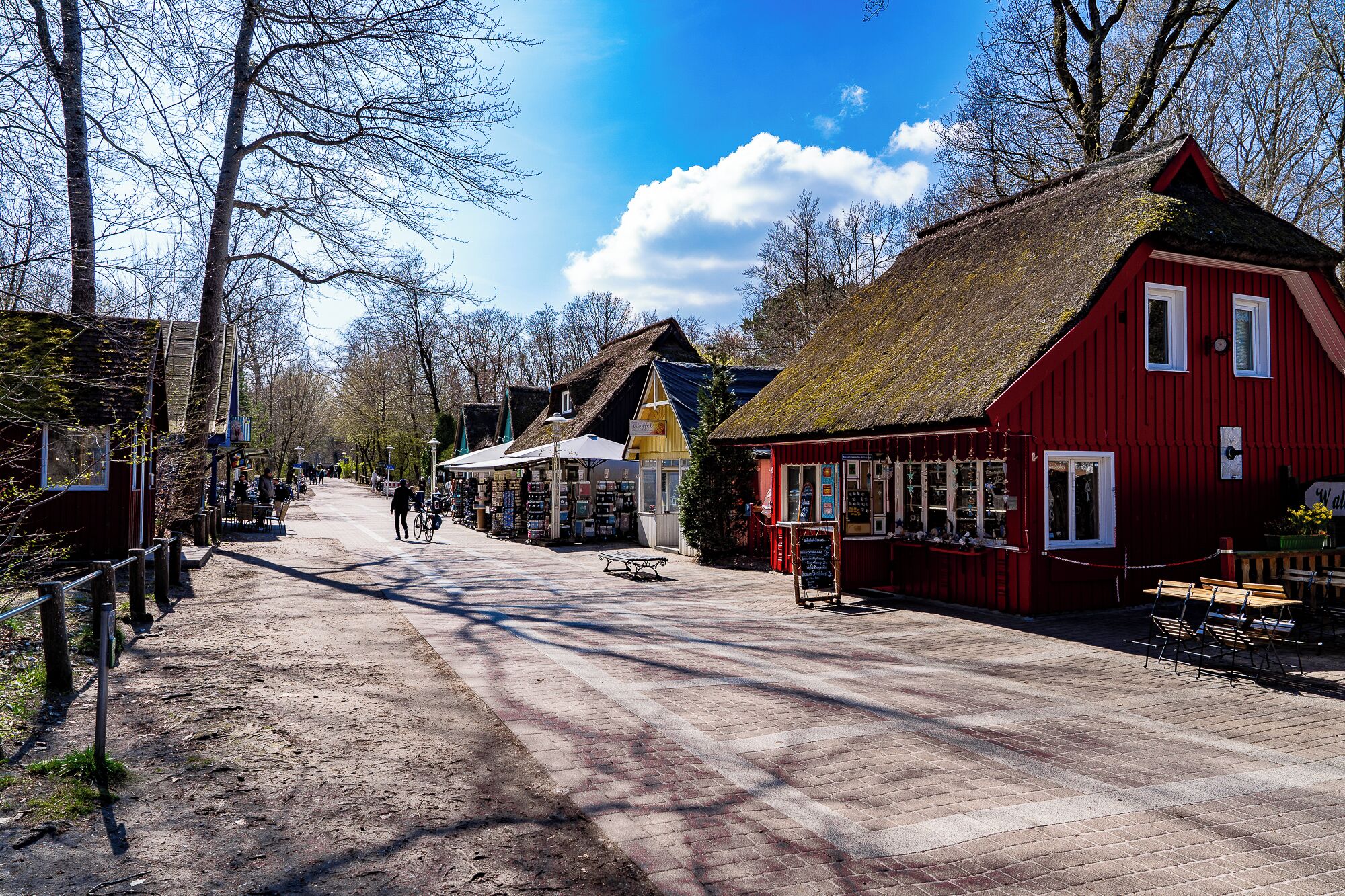A cobblestone street lined with traditional buildings, including a red building with a thatched roof.