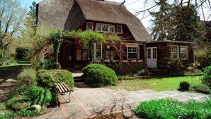 A traditional house with a thatched roof, a front porch, and a small garden with a bench. - Our attractive vacation apartment for 2 people with excellent facilities. (Prerow)
