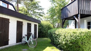 A building with a white exterior and dark brown doors, a bicycle parked in front, and a well-maintained hedge. - Our attractive vacation apartment for 2 people with excellent facilities. (Prerow)