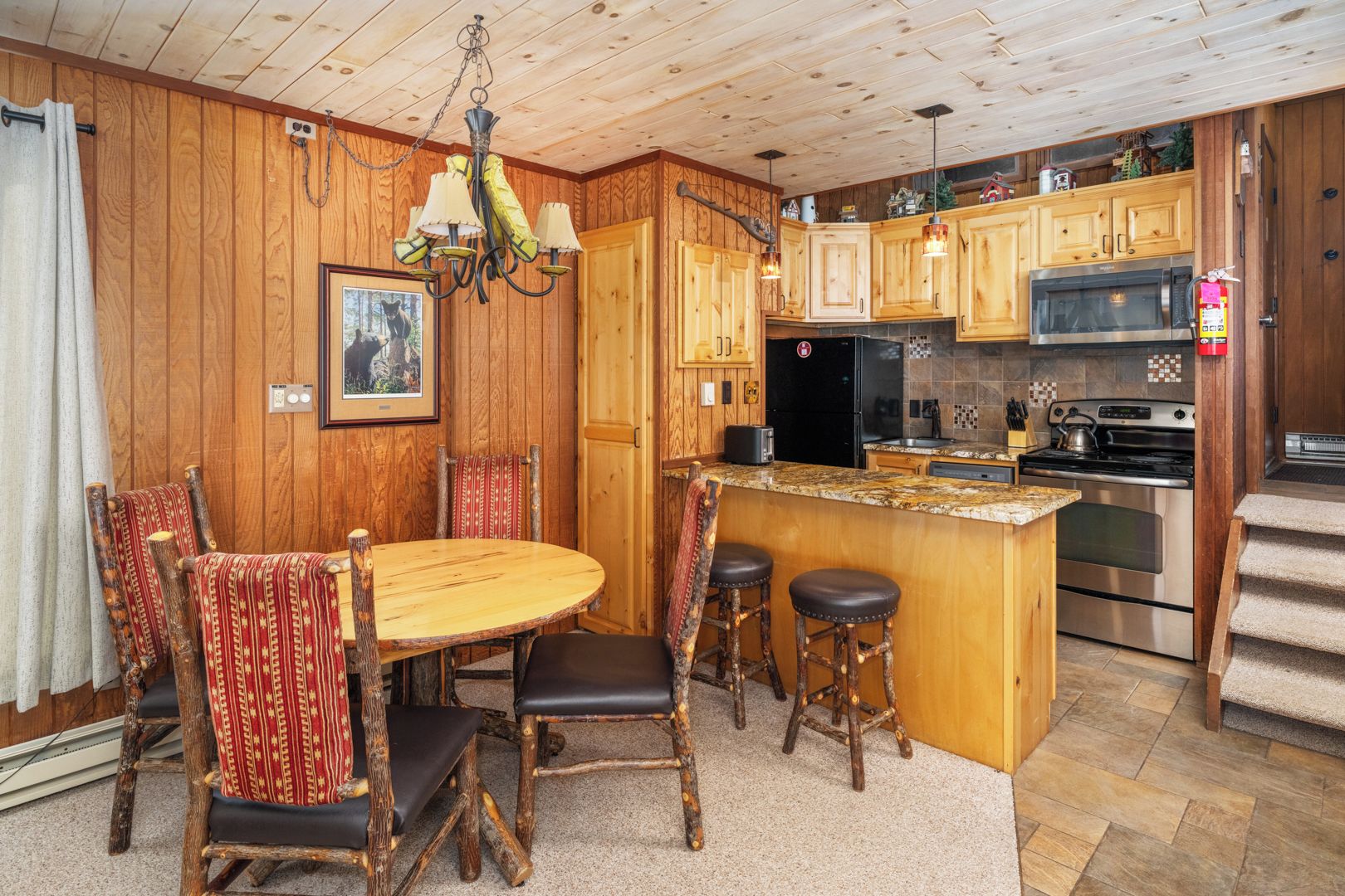 A wooden-paneled kitchen with a central island, bar stools, and a chandelier.