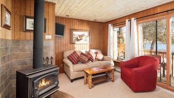 A cozy living room with a fireplace, a sofa with cushions, a red chair, and a large window with curtains.