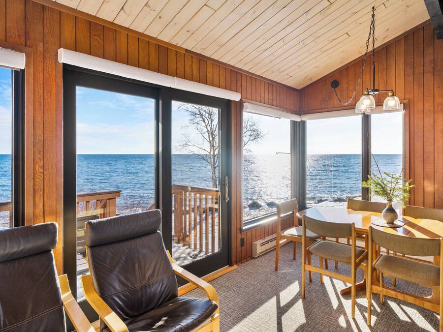 A wooden deck with a table and chairs, a view of the ocean, and a wooden ceiling.