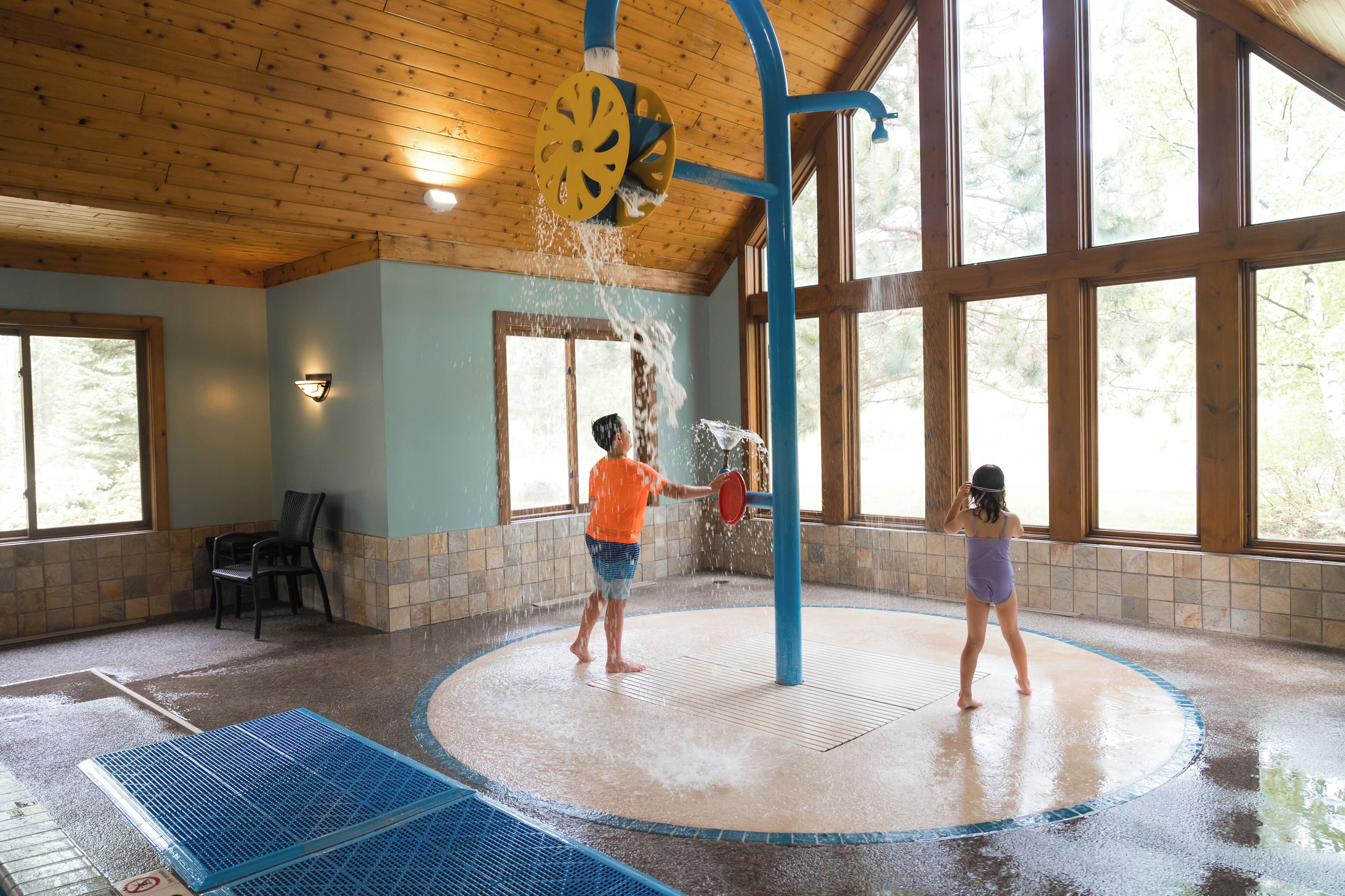 A water play area with a circular pool, a blue play structure, and large windows.