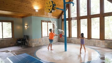 A water play area with a circular pool, a blue play structure, and large windows.