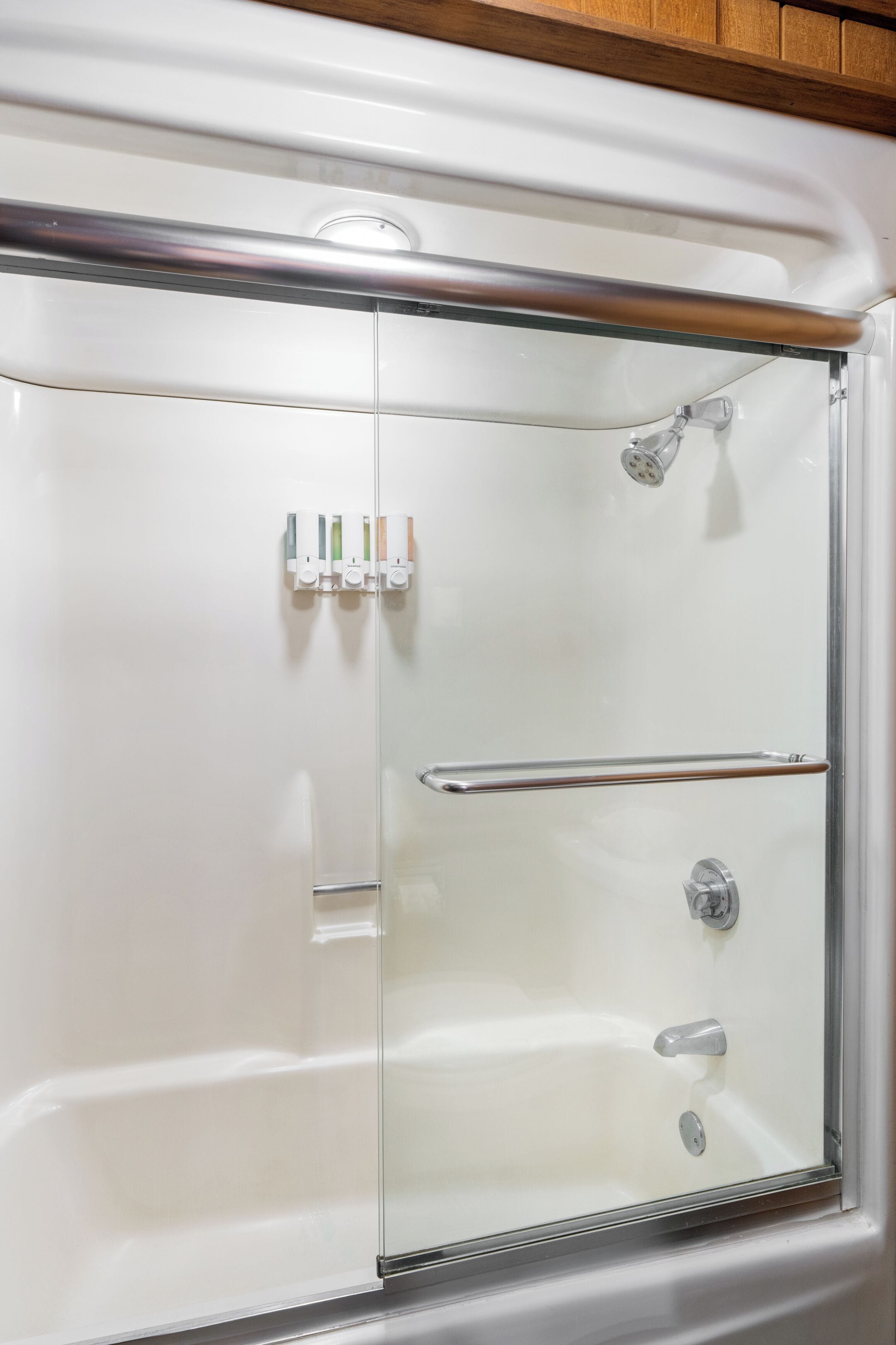 A glass-enclosed shower stall with a handrail, a showerhead, and a control knob.