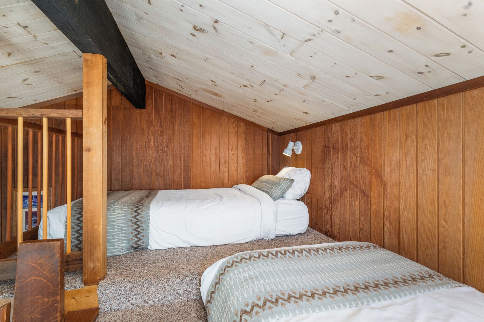 Un dormitorio acogedor con techo inclinado, paredes de madera, una litera y un pequeño escritorio.