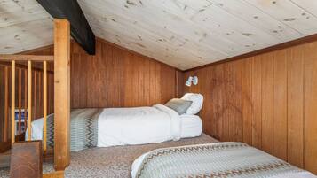 Un dormitorio acogedor con techo inclinado, paredes de madera, una litera y un pequeño escritorio.