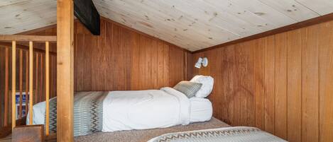A cozy bedroom with a sloped ceiling, wooden walls, a bunk bed, and a small desk.