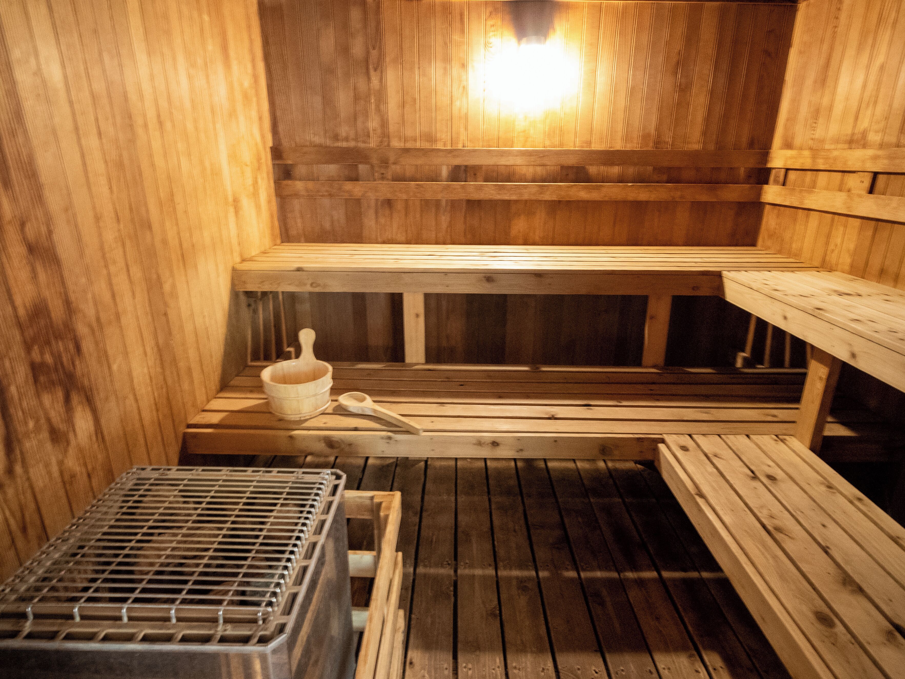 A sauna room with wooden benches, a small table, and a metal container.