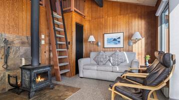 Una habitación acogedora con chimenea, un sofá, un sillón reclinable y una escalera.